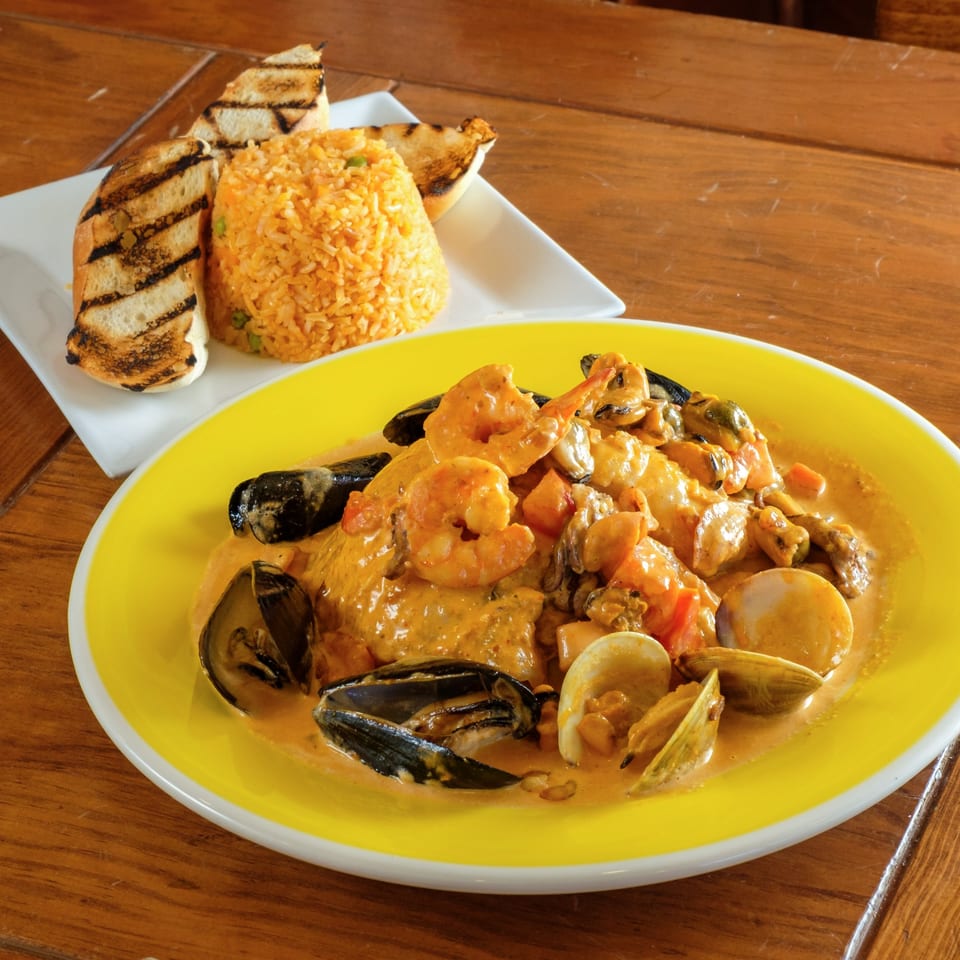 Plaza Garibaldi's seafood dish with shrimp, mussels, and clams in a creamy sauce, served with rice and grilled bread.