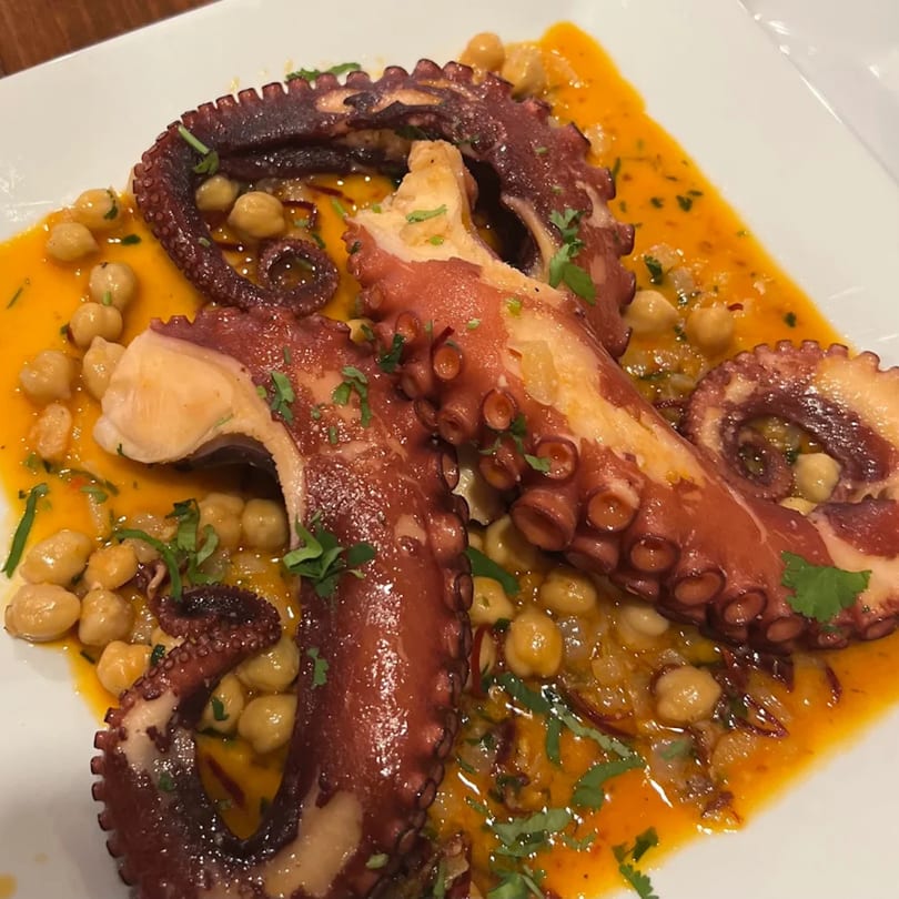 Grilled octopus tentacles with chickpeas and a vibrant orange sauce, garnished with fresh herbs.