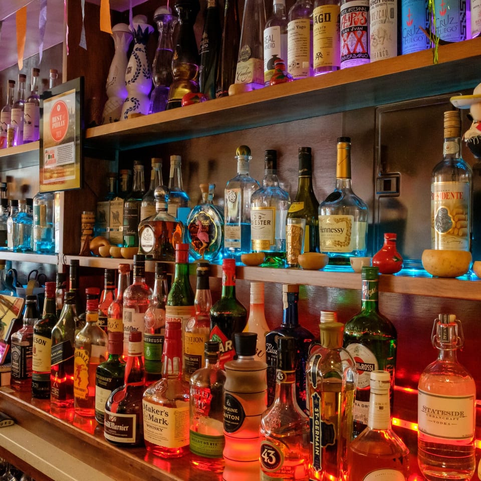 A vibrant bar shelf at Plaza Garibaldi Mezcaleria, filled with various liquor bottles and colorful lighting.