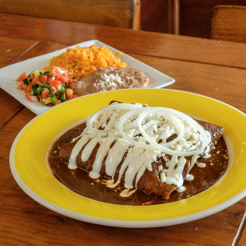 Plaza Garibaldi Mezcaleria's enchiladas with mole, sour cream, onions, rice, beans, and pico de gallo.