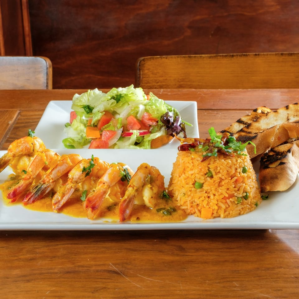 Plaza Garibaldi Mezcaleria's shrimp dish with rice, salad, and grilled bread on a wooden table.