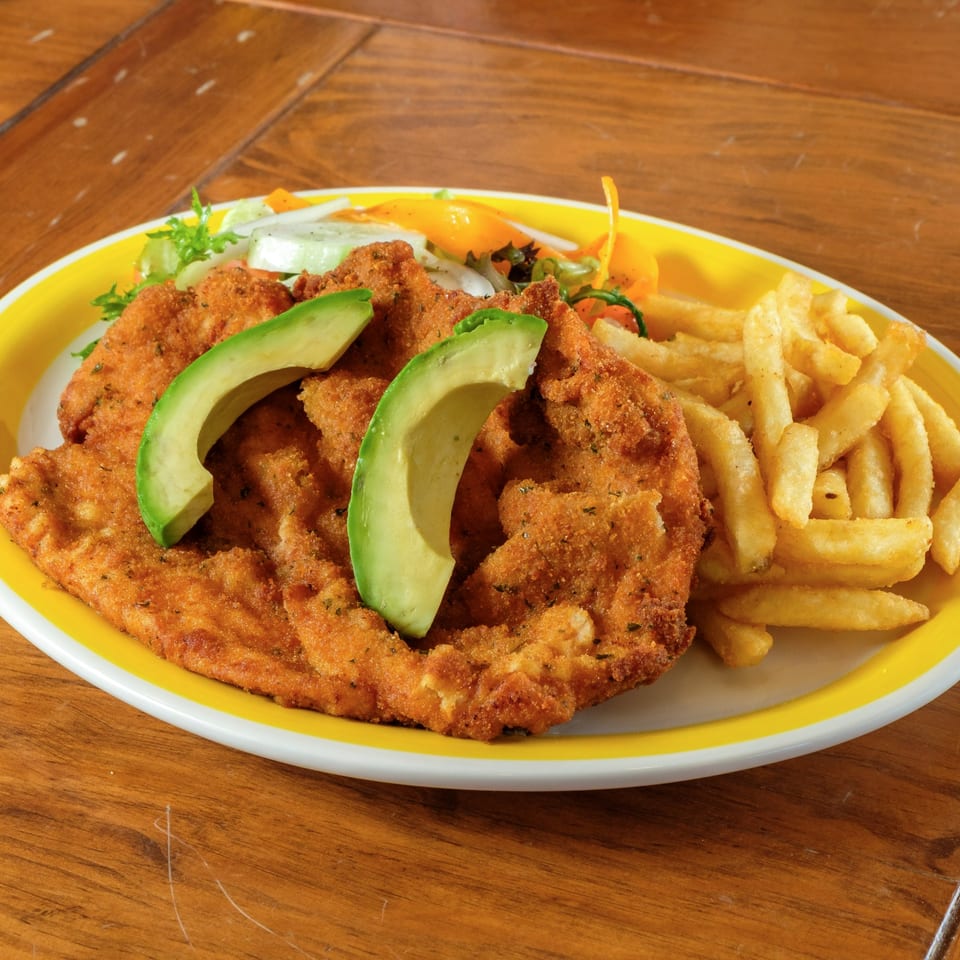 Plaza Garibaldi Mezcaleria's milanesa with avocado slices, french fries, and a side salad on a yellow plate.
