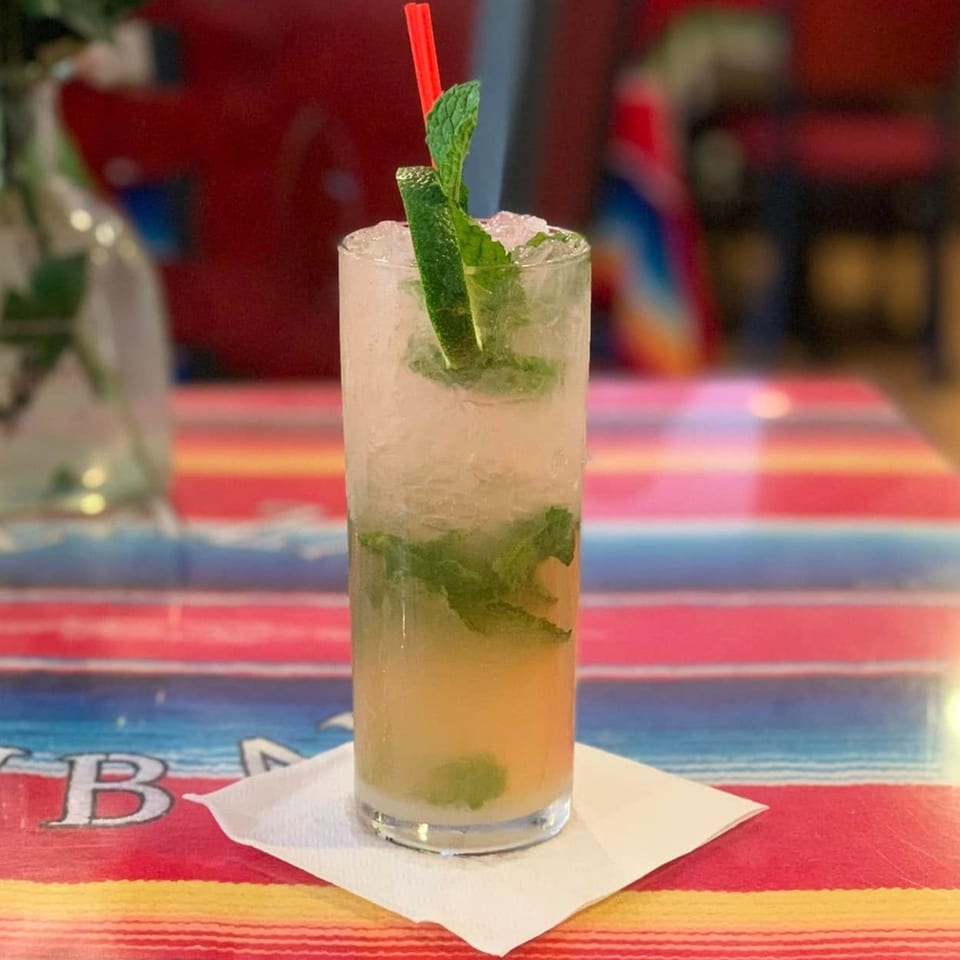 A refreshing mojito with mint and lime, served in a tall glass on a colorful striped table.