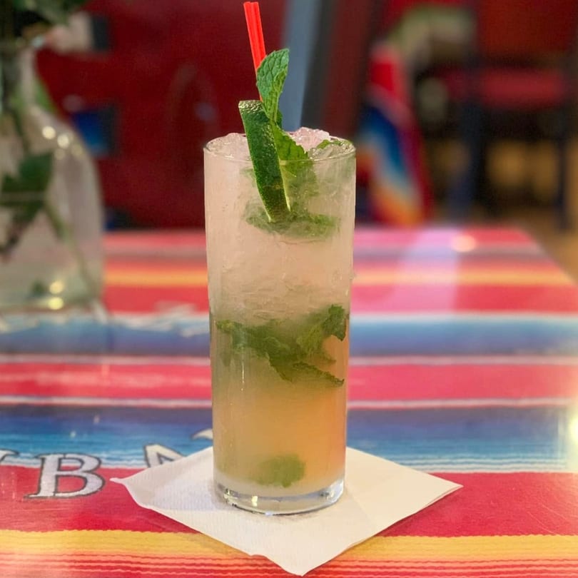 A refreshing mojito with mint and lime, served in a tall glass on a colorful striped table.