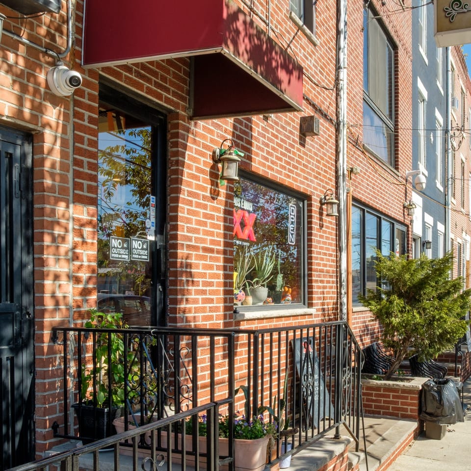 Exterior of Plaza Garibaldi Mezcaleria, a brick building with a red awning and potted plants.