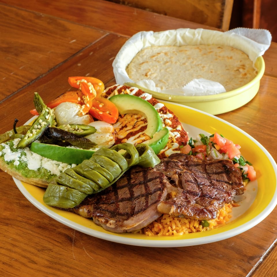 Plaza Garibaldi Mezcaleria's grilled steak with rice, vegetables, and tortillas on a wooden table.