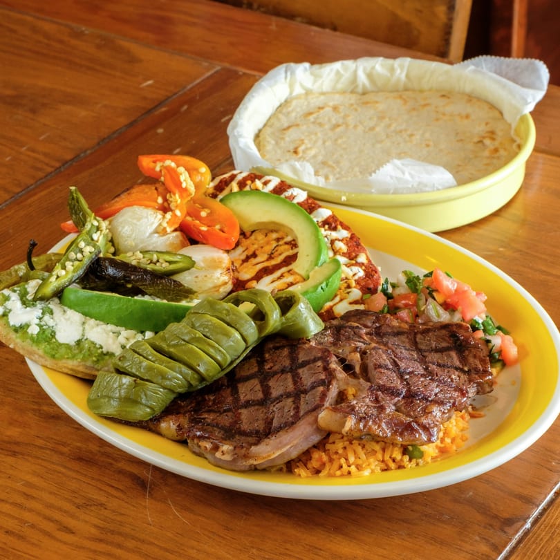 Plaza Garibaldi Mezcaleria's grilled steak with rice, vegetables, and tortillas on a wooden table.