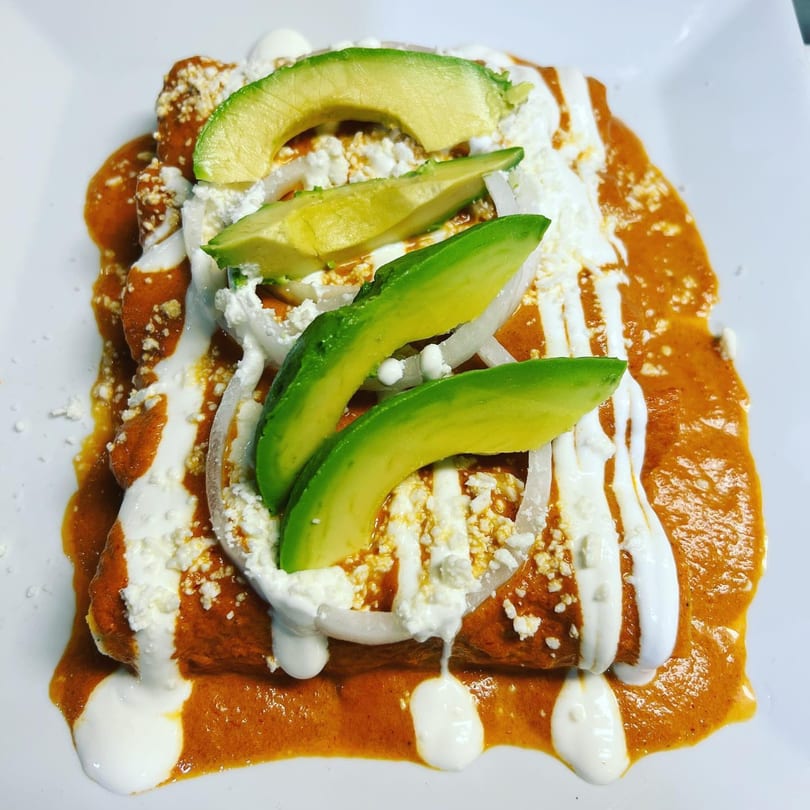 Plaza Garibaldi Mezcaleria's enchiladas with red sauce, sour cream, crumbled cheese, onions, and avocado slices.